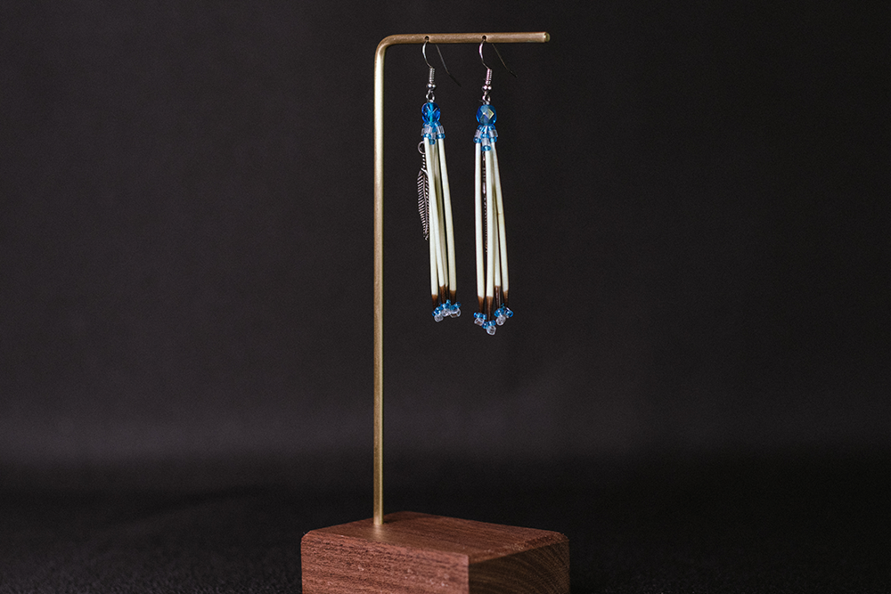 Hand-made earrings made with porcupine needles, blue beads, and a feather accent