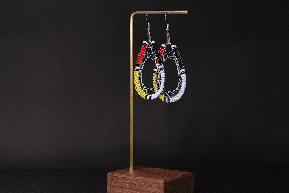 Hand-made teardrop hoop earrings with woven webbing and yellow, black, white, and ted beads.