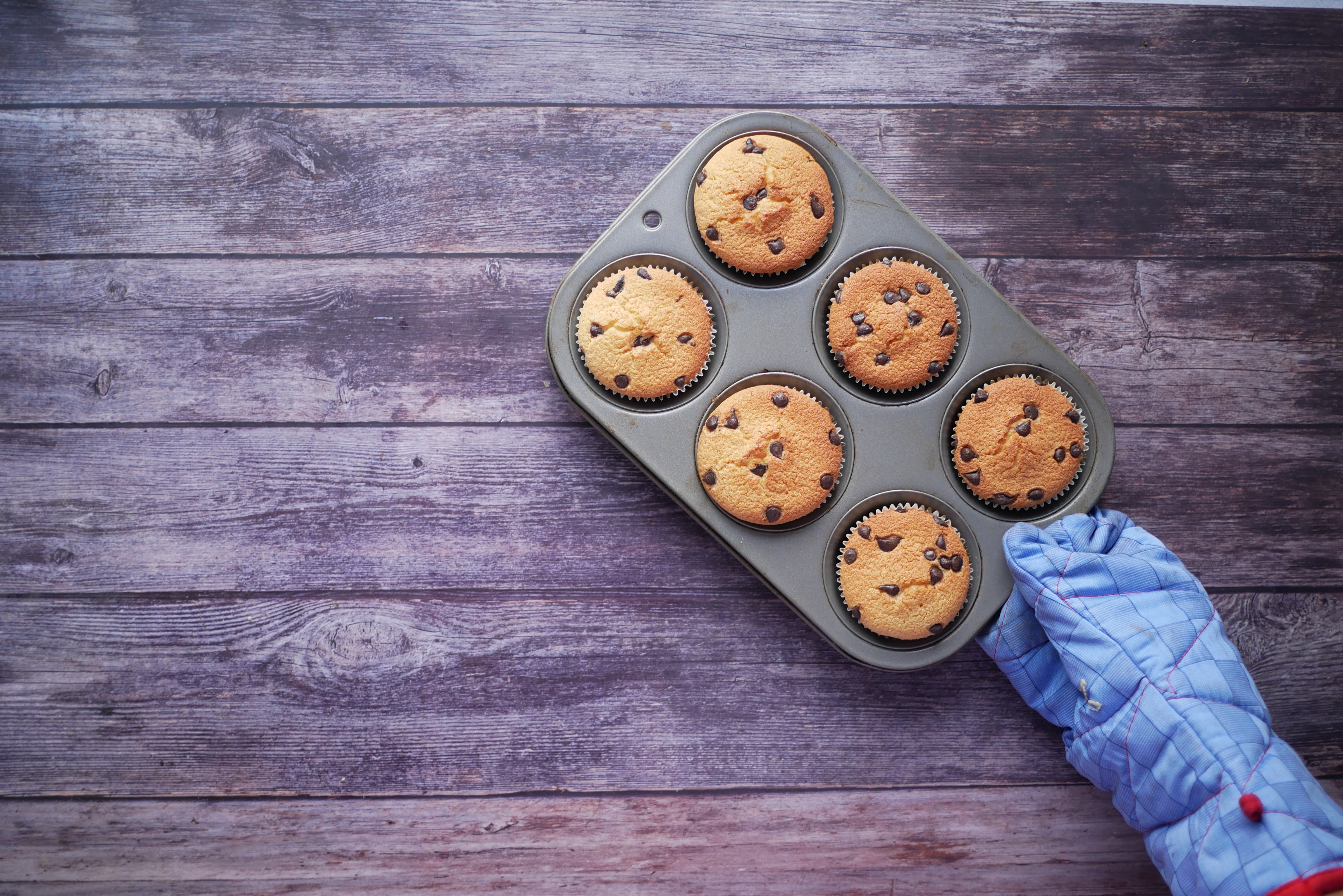 On a wooden table, a half dozen of freshly made chocolate-chip muffins rests.