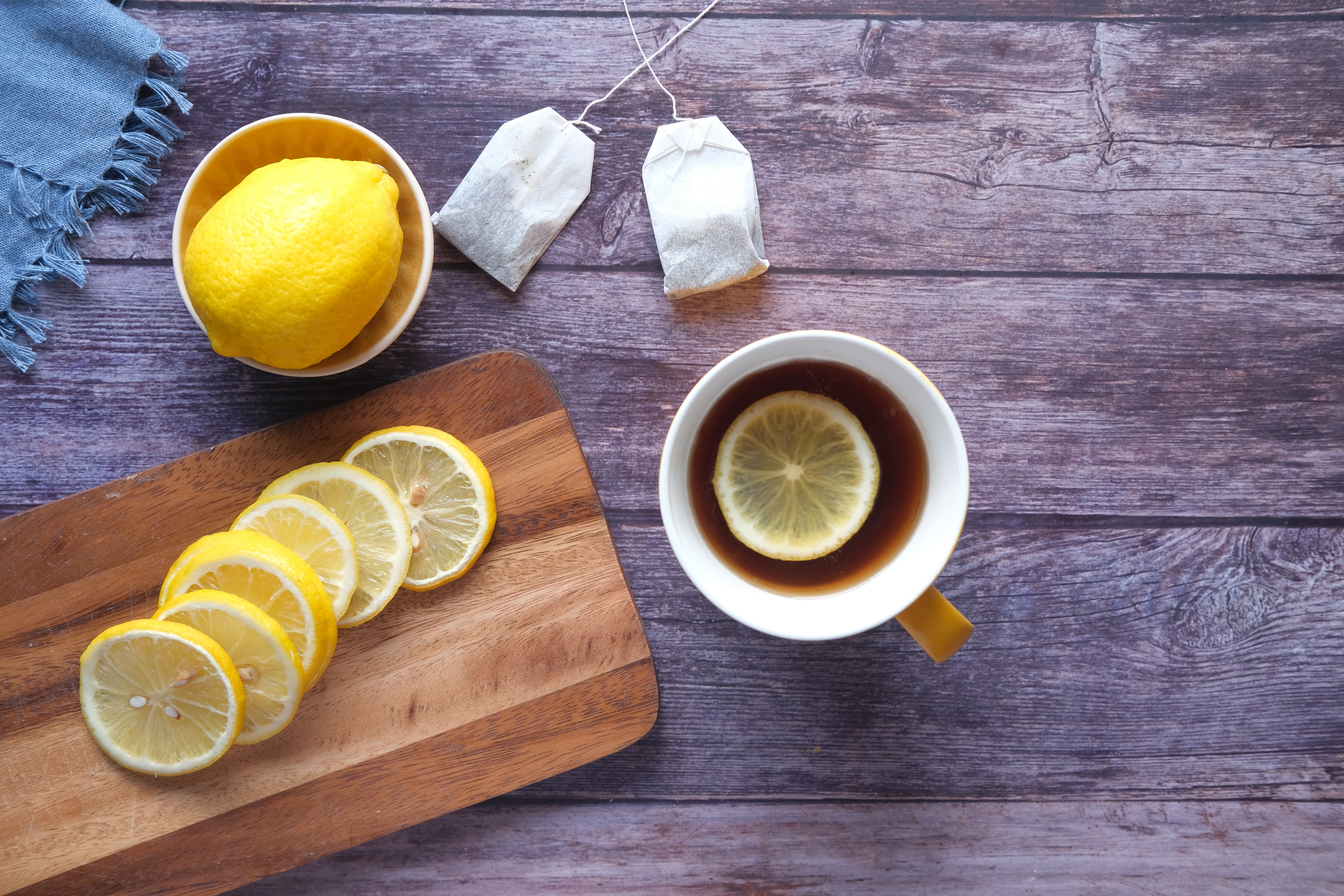 On a wood table, a white mug with a freshly steeped tea and a fresh cut lemon