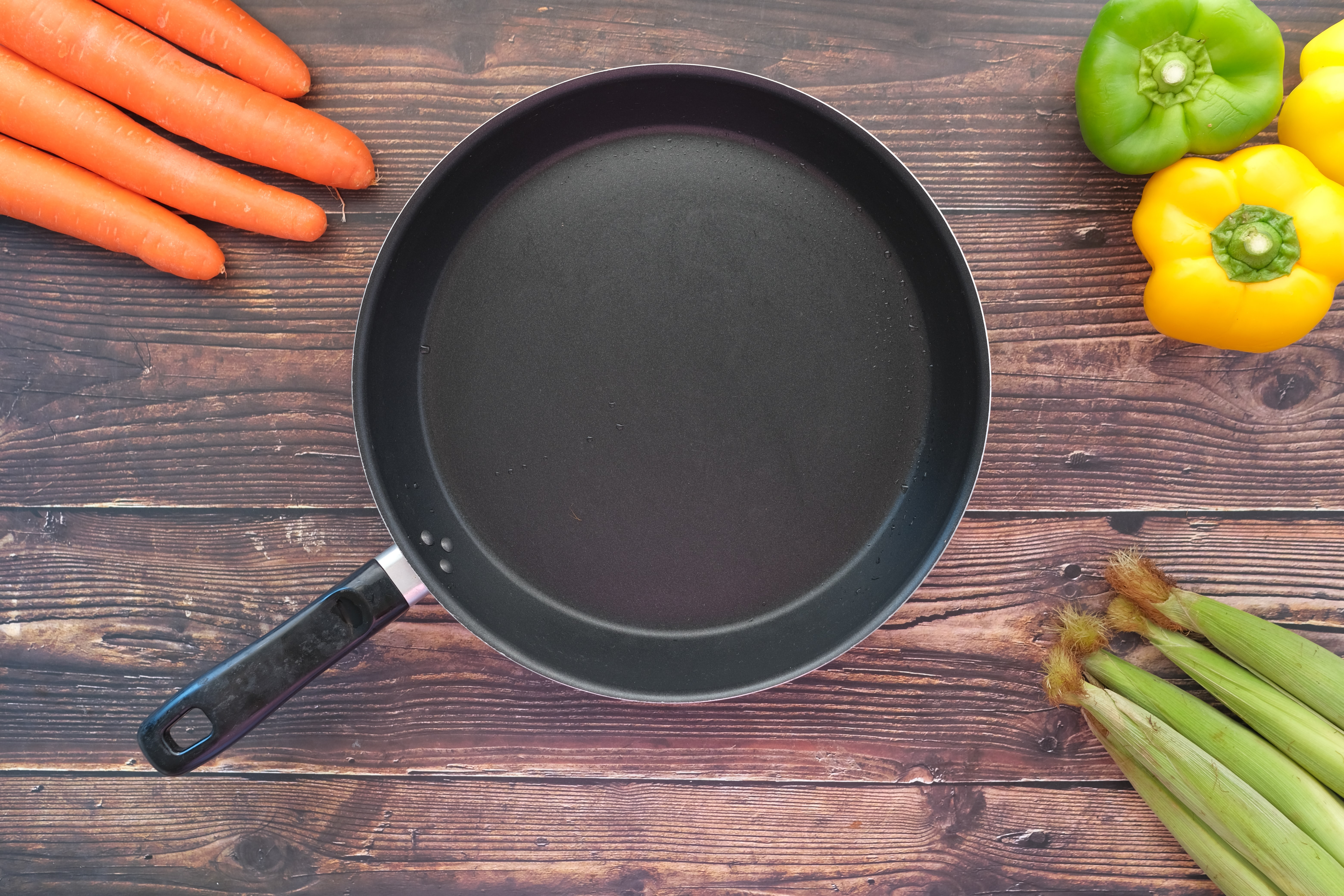 Decorative photo of a pan on a wood counter with various fresh vegetables.